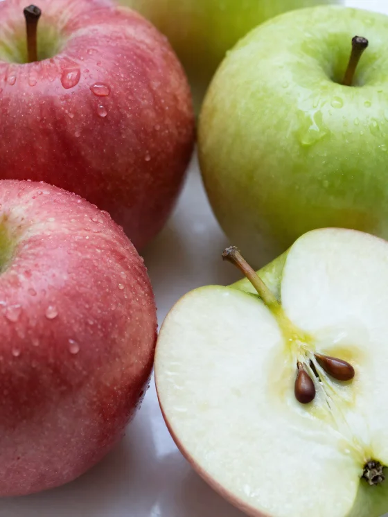 Fresh red and green apples on a chopping board, sliced and whole, with apple juice