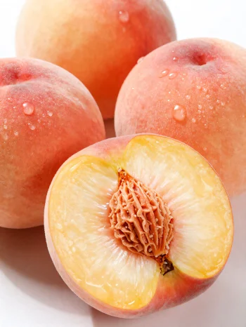 Whole and sliced peaches on a wooden table next to a glass of peach juice