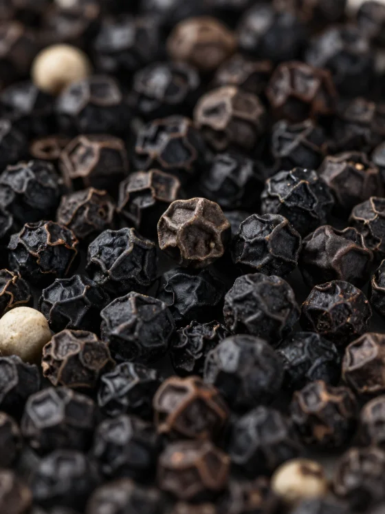 Black peppercorns and ground pepper in a ceramic bowl and on a wooden surface