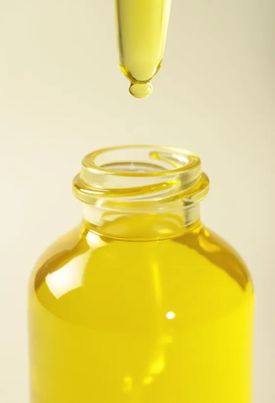 Lemon oil in a small bottle beside fresh lemon slices and zest