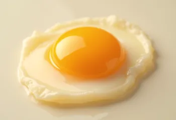 Separated raw egg yolks in a glass bowl on wood