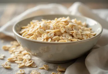 Raw rolled oats in a ceramic bowl scattered on wood